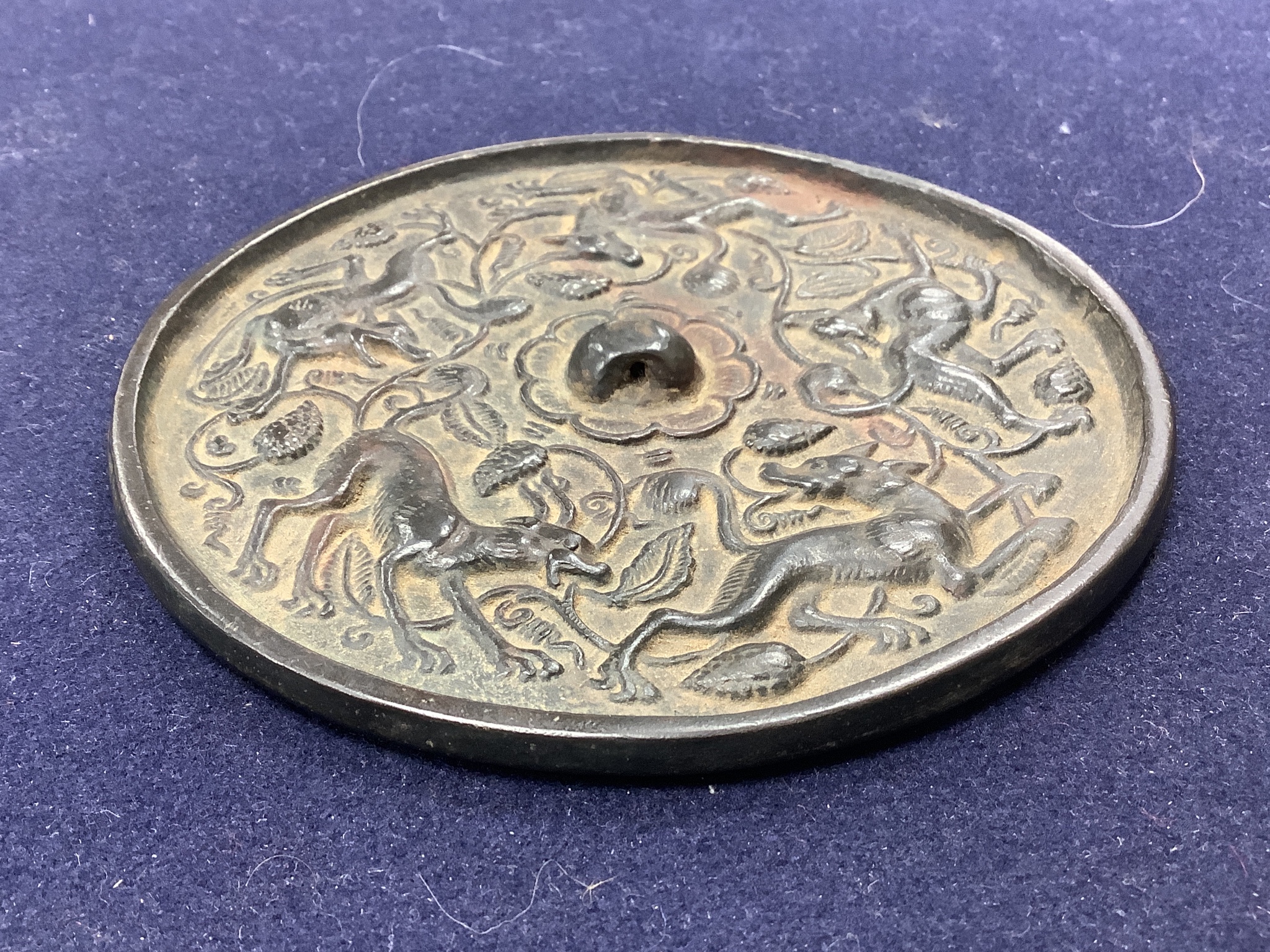 A Chinese bronze mirror, cast with vines and hounds, 14cm